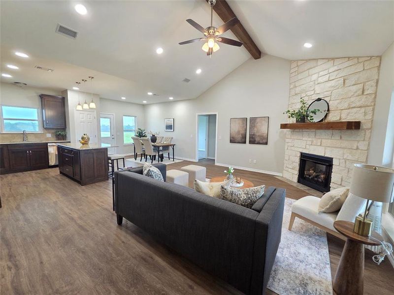Living room featuring wood finished floors, beamed ceiling, plenty of natural light, a fireplace, and a ceiling fan Living room featuring wood finished floors, beamed ceiling, plenty of natural light, a fireplace, and a ceiling fan