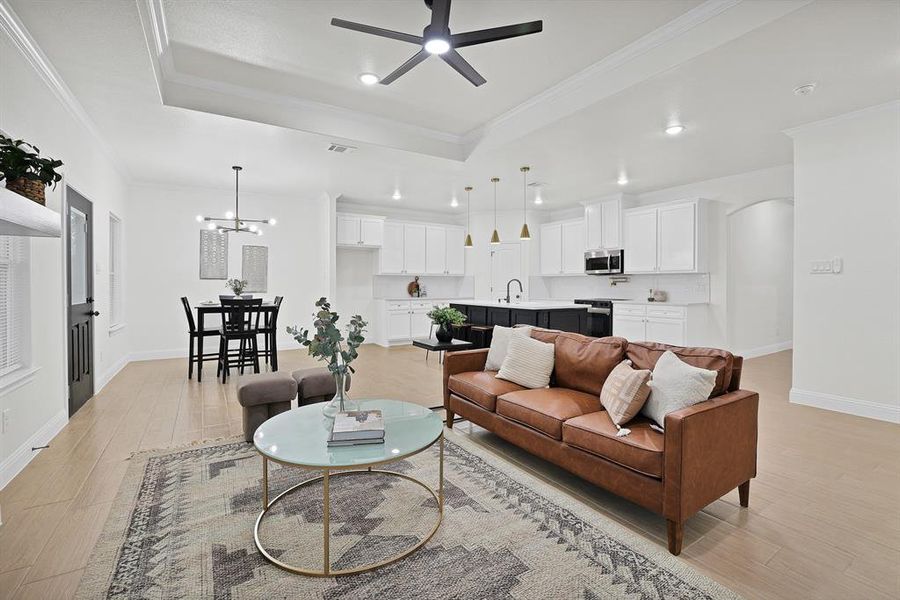 Living room with ceiling fan with notable chandelier, light wood-type flooring, crown molding, and sink