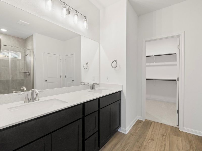 A well-lit primary bathroom features a dual vanity and an adjacent walk-in closet.