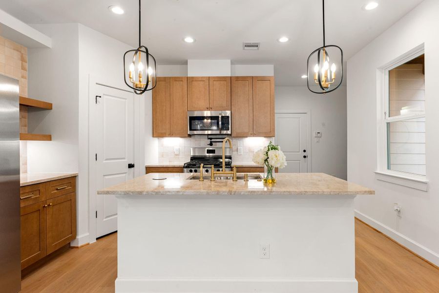 Expansive quartz island serving as the centerpiece of the kitchen, featuring a designer gooseneck faucet, ample prep space, and seating potential. Framed by warm wood cabinetry, stainless steel appliances, and modern pendant lighting, this space blends style with everyday functionality.