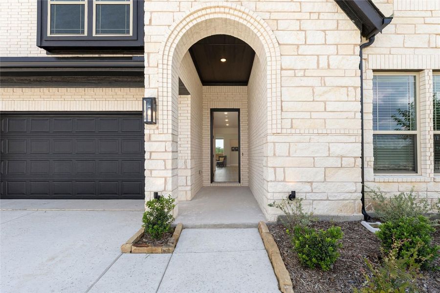 Stone home entrance with arched brick entryway, dark front door, and two-car garage