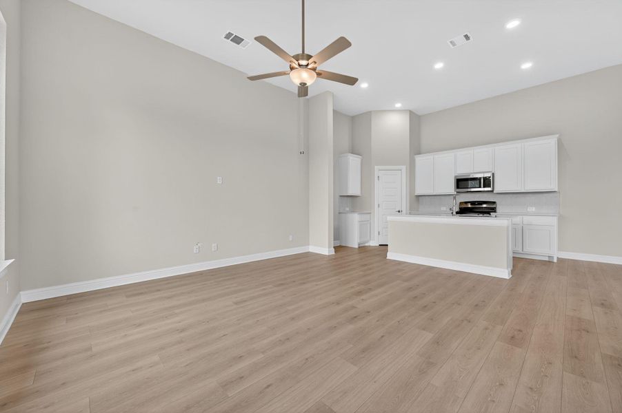 Unfurnished living room with light wood-style flooring, a ceiling fan, recessed lighting, and a towering ceiling