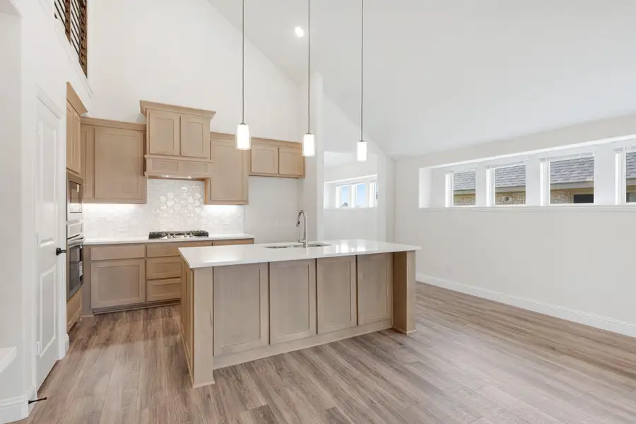 Kitchen with light wood cabinets, large island with sink, vaulted ceiling, and pendant lights over hardwood floors