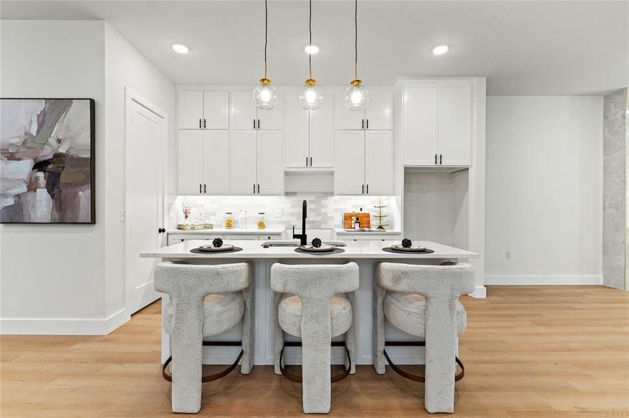 Kitchen featuring white cabinets, decorative light fixtures, light wood-type flooring, decorative backsplash, and a breakfast bar Kitchen featuring white cabinets, decorative light fixtures, light wood-type flooring, decorative backsplash, and a breakfast bar