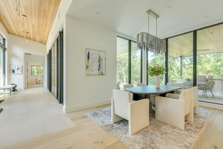 Natural light floods this dining area, featuring a linear chandelier and expansive glass doors opening to the outdoors. Natural light floods this dining area, featuring a linear chandelier and expansive glass doors opening to the outdoors.