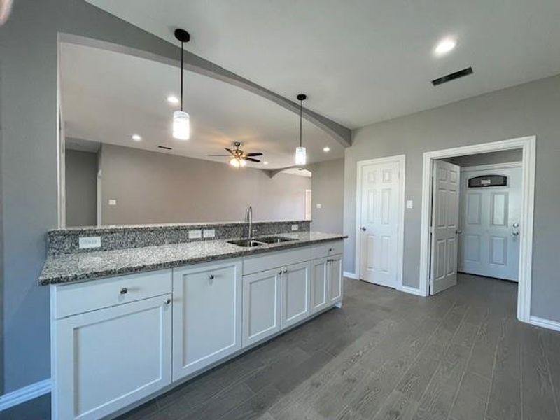 Kitchen with white cabinets, granite counters, ceramic wood-look flooring, decorative light fixtures, and a sink Kitchen with white cabinets, granite counters, ceramic wood-look flooring, decorative light fixtures, and a sink