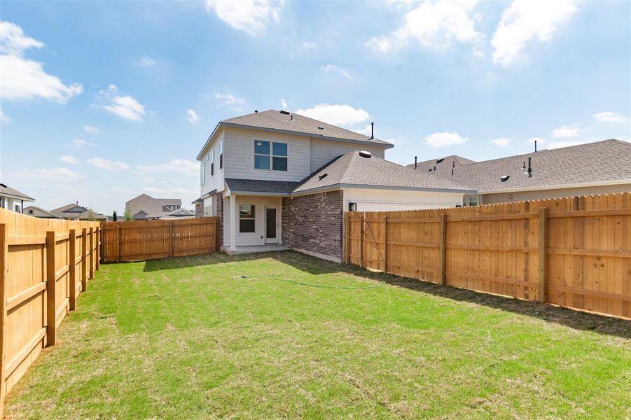 Rear view of property with a fenced backyard, brick siding, roof with shingles, and a lawn