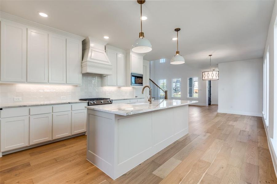 Kitchen featuring decorative backsplash, custom range hood, a kitchen island with sink, black microwave, and light hardwood / wood-style floors