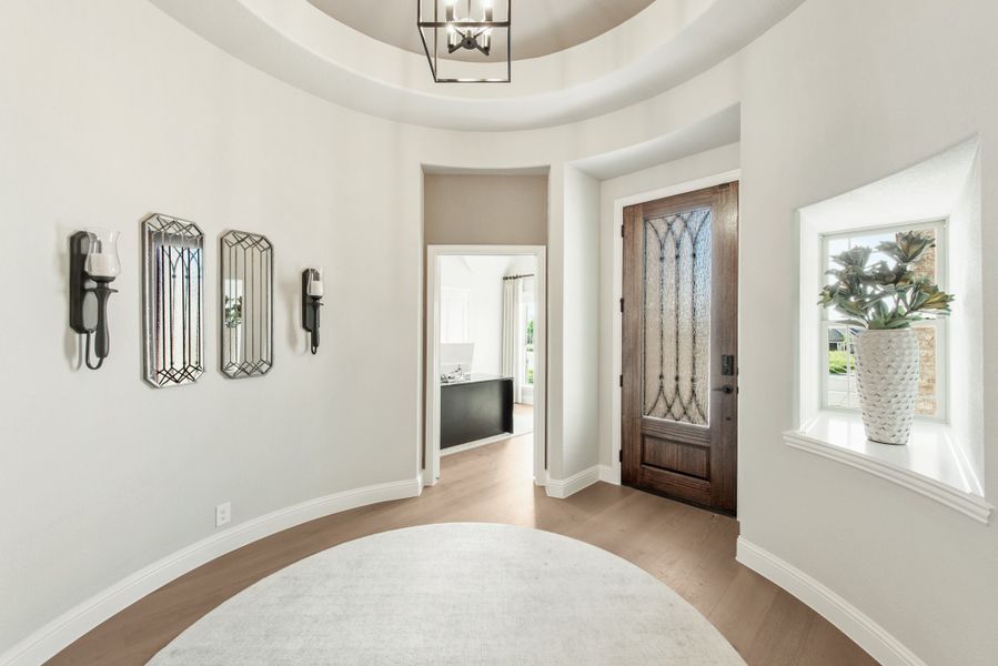 Round foyer with tray ceiling, chandelier, wood front door with glass panel, and hardwood floors