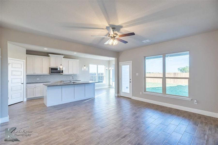 Kitchen featuring white cabinets, light wood-style flooring, stainless steel microwave, open floor plan, and recessed lighting