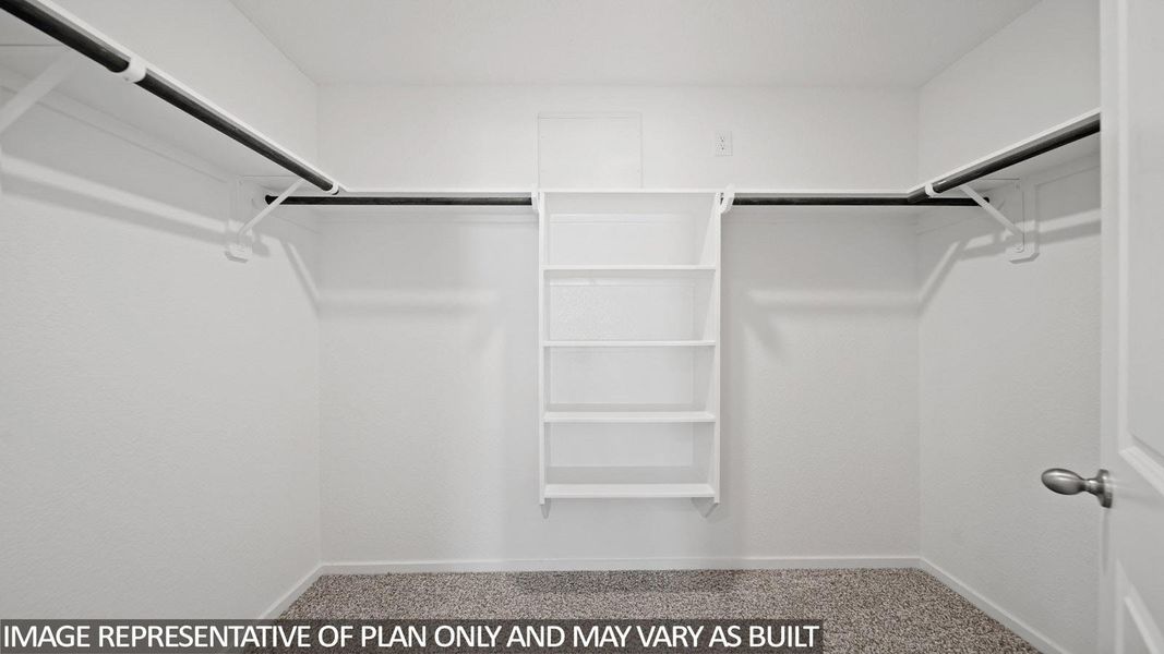Walk-in closet with integrated shelving system, multiple hanging rods, and textured carpet flooring