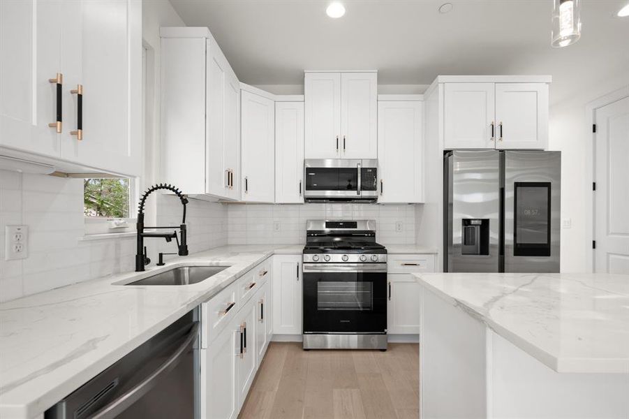 Kitchen featuring stainless steel appliances, white cabinetry, light stone countertops, backsplash, and light wood-type flooring