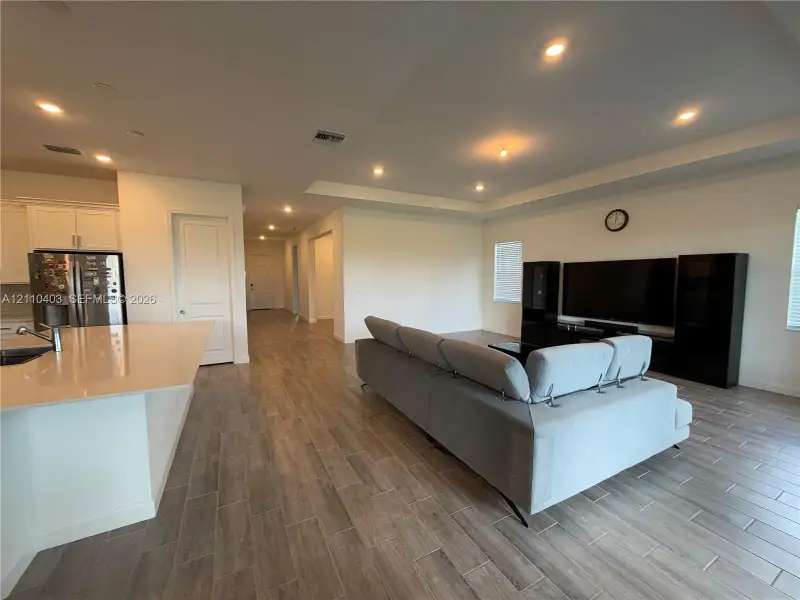 Open-concept interior featuring wood-finish tile flooring, recessed ceiling lighting, a tray ceiling, and a large island with a countertop