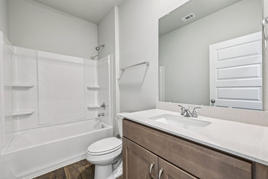 Image of a bathroom with a vanity, brown cabinets, a mirror and a shower with a tub