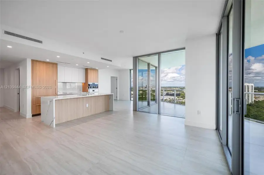 Open-concept kitchen featuring wood-finish cabinetry, a waterfall-edge stone island, built-in stainless steel appliances, wood-finish flooring, and floor-to-ceiling glass doors