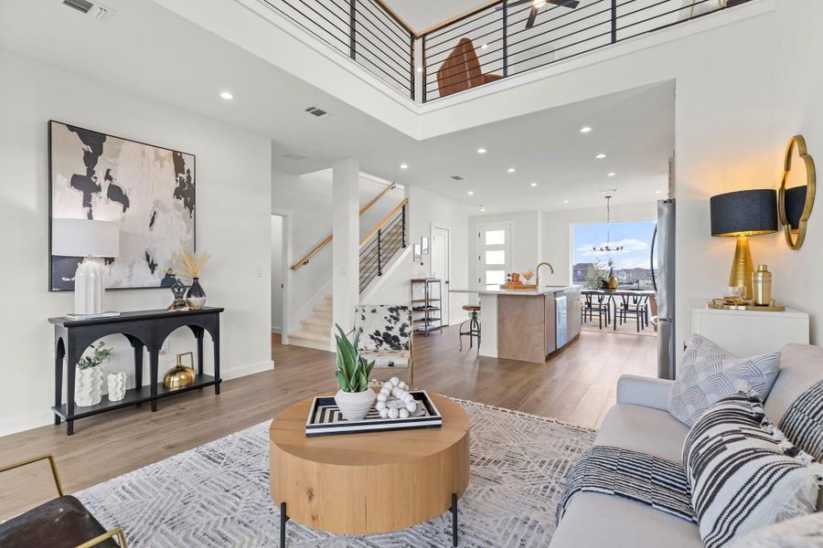 Living room featuring light wood-style flooring, a high ceiling, and suspended lighting