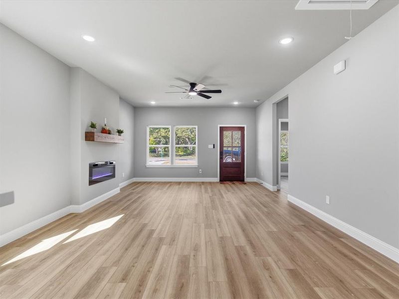 Unfurnished living room featuring a glass covered fireplace, recessed lighting, light wood-style flooring, ceiling fan, and attic access Unfurnished living room featuring a glass covered fireplace, recessed lighting, light wood-style flooring, ceiling fan, and attic access