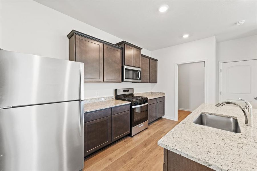 Kitchen featuring appliances with stainless steel finishes, sink, dark cabinets, and light wood-style floors