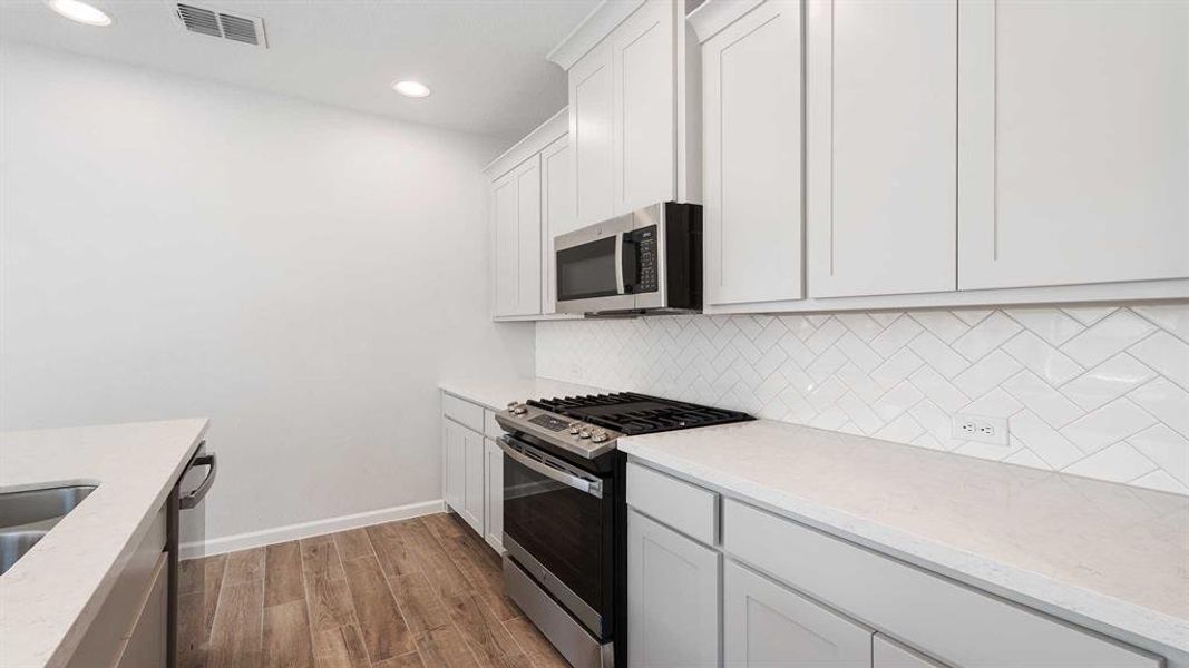 Kitchen featuring light stone counters, decorative backsplash, appliances with stainless steel finishes, white cabinets, and light hardwood / wood-style floors