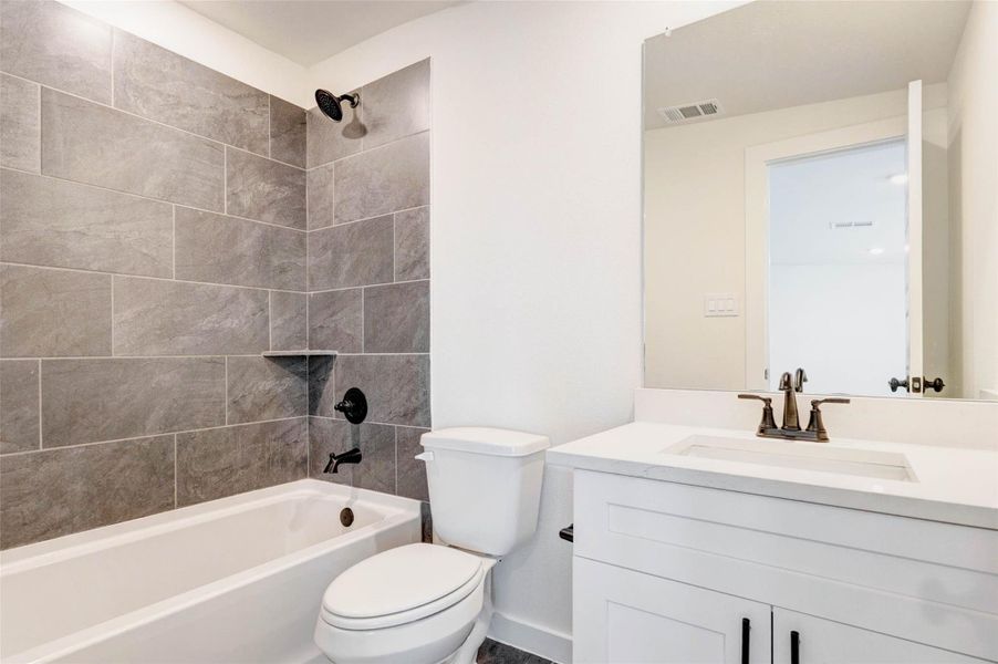 This well-appointed secondary bathroom features a clean, modern design with a tub and shower combination surrounded by stylish tile work. A sleek vanity with quartz countertops and contemporary fixtures offers both functionality and elegance. The large mirror enhances light and space, creating a bright and inviting environment that is perfect for guests or everyday use.