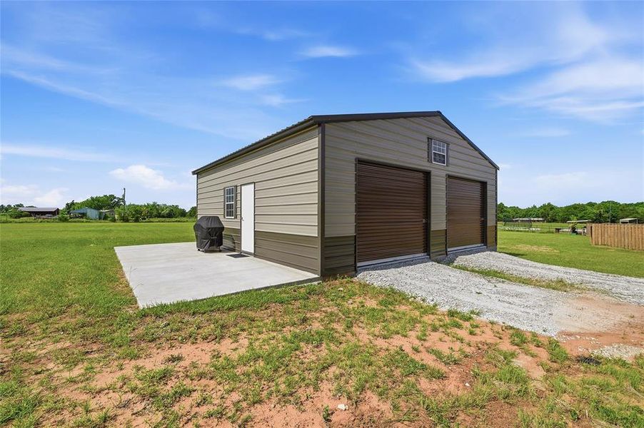 Two-tone metal outbuilding featuring two roll-up garage doors, a pedestrian entry door, and a single-pane window