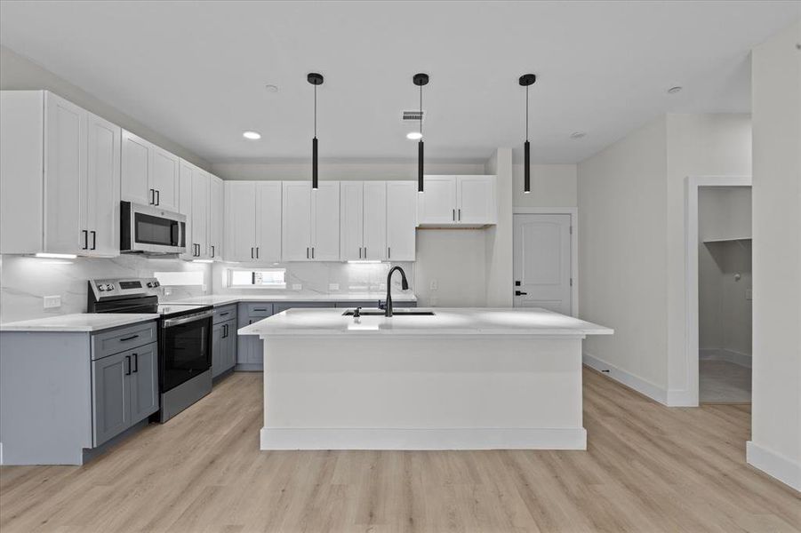 Kitchen with stainless steel appliances, light wood-type flooring, an island with sink, gray cabinetry, and recessed lighting