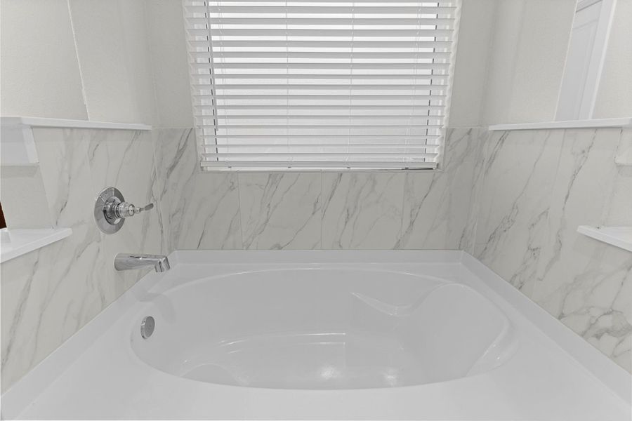 A closer look at the soaking tub reveals its luxurious design, surrounded by a marble-look tile surround that adds a touch of timeless elegance to this serene space. A closer look at the soaking tub reveals its luxurious design, surrounded by a marble-look tile surround that adds a touch of timeless elegance to this serene space.