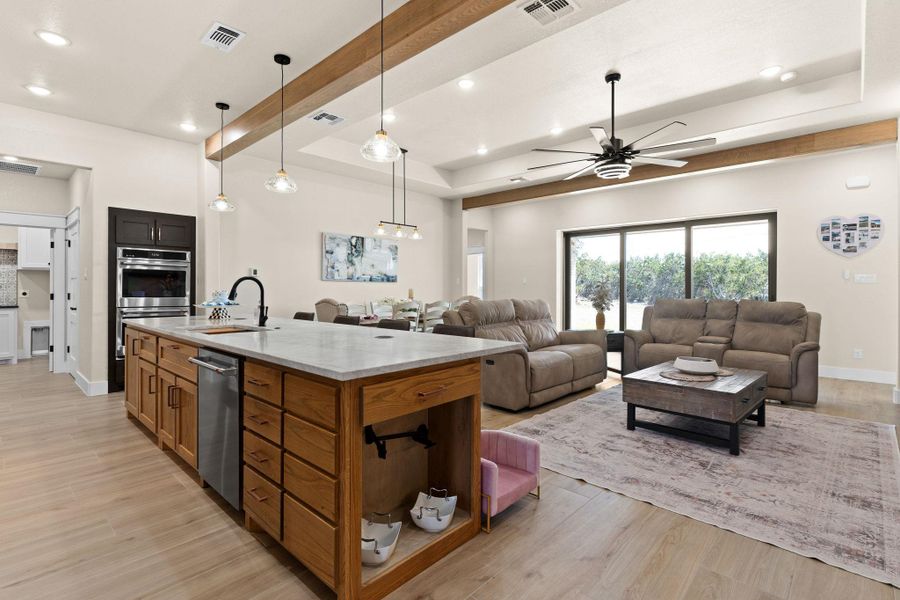 Kitchen featuring a raised ceiling, a sink, appliances with stainless steel finishes, open floor plan, and light stone counters Kitchen featuring a raised ceiling, a sink, appliances with stainless steel finishes, open floor plan, and light stone counters