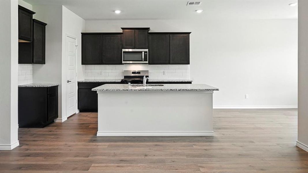 Kitchen with stainless steel appliances, light stone counters, a center island with sink, dark wood-style flooring, and tasteful backsplash