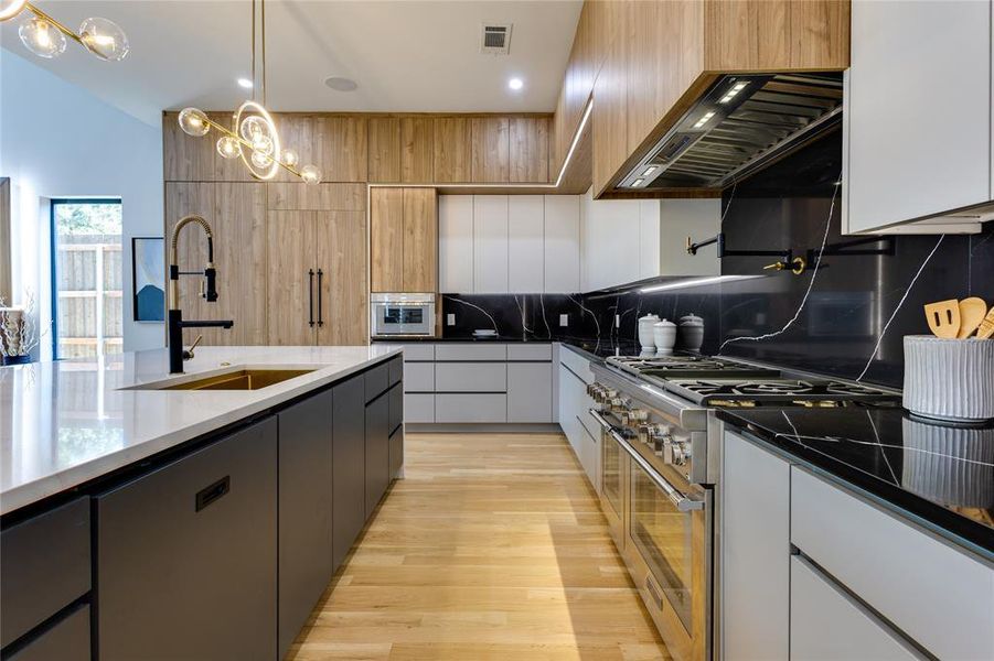 Kitchen with custom exhaust hood, white cabinetry, backsplash, light wood-type flooring, and stainless steel stove