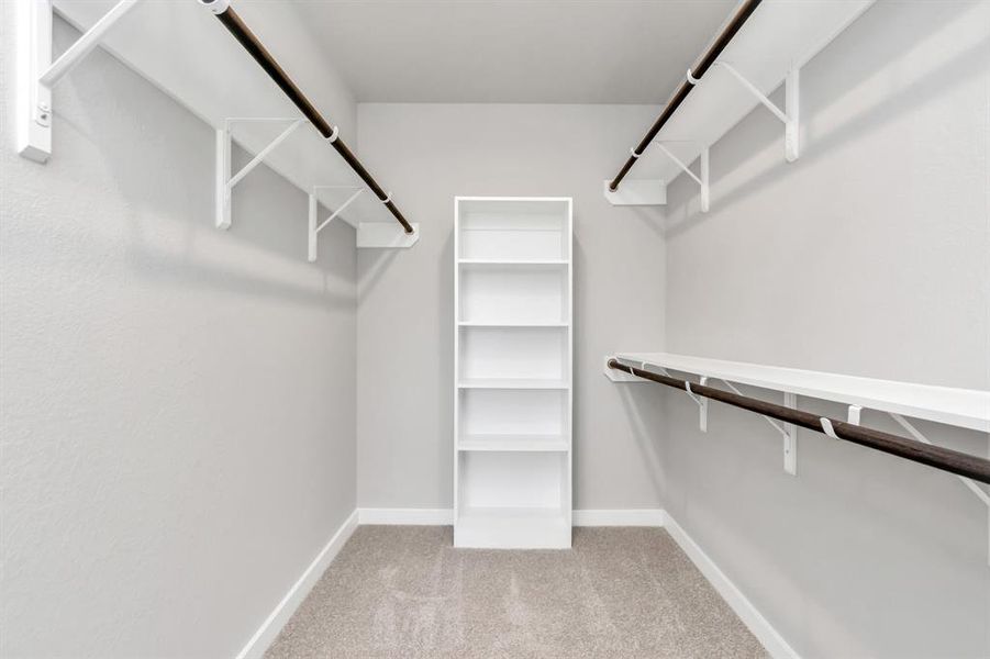 Experience luxury in this spacious walk-in closet with high ceilings and plush carpet. Warm paint tones, built-in shelving, recessed lighting, and dark finishes create a contemporary and functional retreat.  Sample photo of completed plan. As-built color and selections may vary.