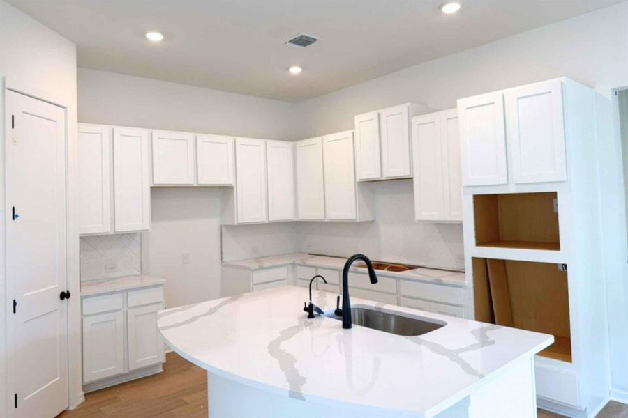 Kitchen with white cabinetry, wood finished floors, a center island with sink, light stone counters, and recessed lighting