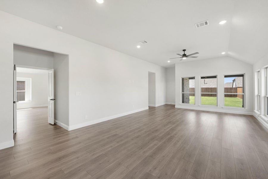 Open living room with vaulted ceiling, ceiling fan, hardwood floors, and large windows overlooking backyard Open living room with vaulted ceiling, ceiling fan, hardwood floors, and large windows overlooking backyard