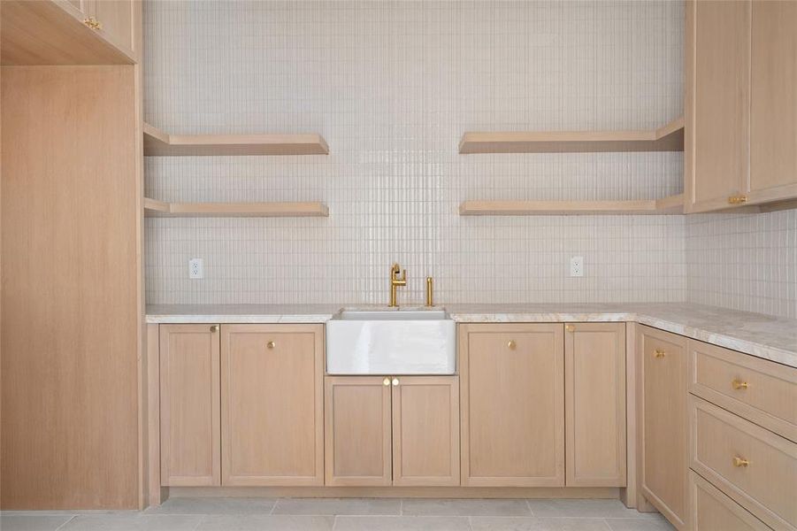 Blending functionality with elegance, the laundry room features marble countertops and a classic farmhouse apron-front sink. Custom-built cabinetry and open shelving provide ample storage, while a skylight fills the space with natural light. The London Gray limestone tile floor adds a refined touch, completing this beautifully designed and highly practical workspace.