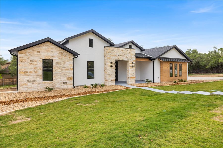 View of front facade featuring stone siding, a standing seam roof and landscaped front yard. View of front facade featuring stone siding, a standing seam roof and landscaped front yard.