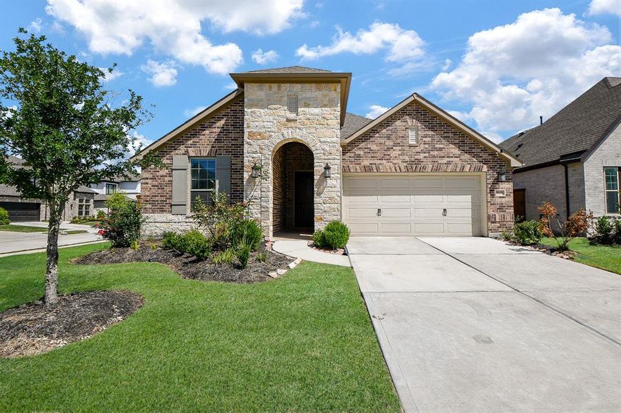 This charming home features a modern brick and stone exterior with a two-car garage. It includes a well-maintained front yard with landscaped garden beds, offering great curb appeal in a pleasant neighborhood setting.