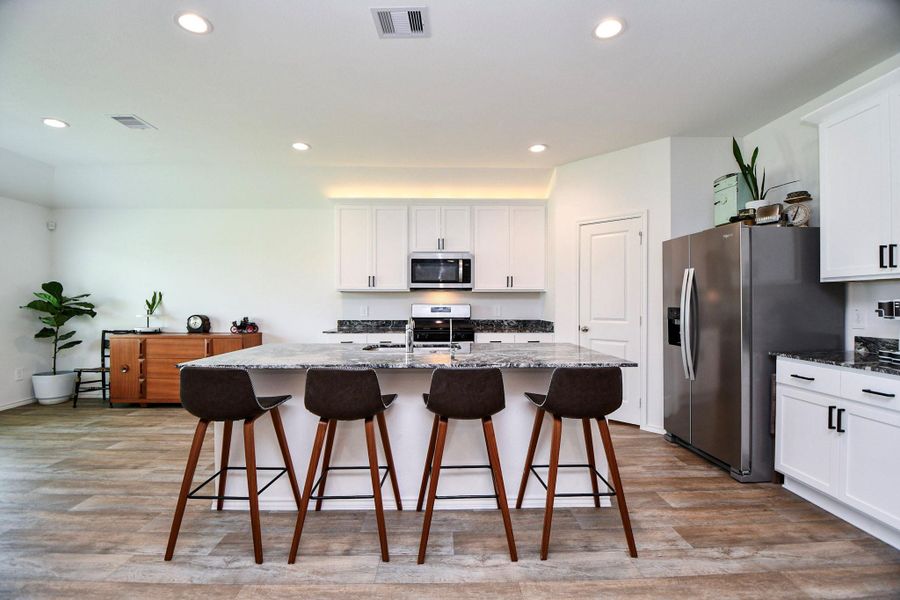 White cabinetry and a large island, seamlessly flowing into the living room. This modern kitchen features a spacious island, sleek stainless-steel appliances, and seating for four.
