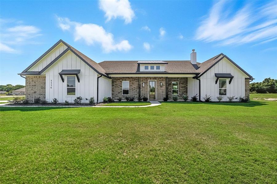 Modern farmhouse featuring board and batten siding, covered porch, a front lawn, and a chimney Modern farmhouse featuring board and batten siding, covered porch, a front lawn, and a chimney