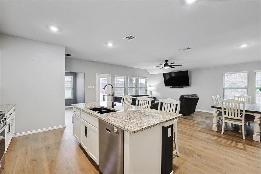 Kitchen with white cabinetry, sink, light stone counters, stainless steel appliances, and a center island with sink