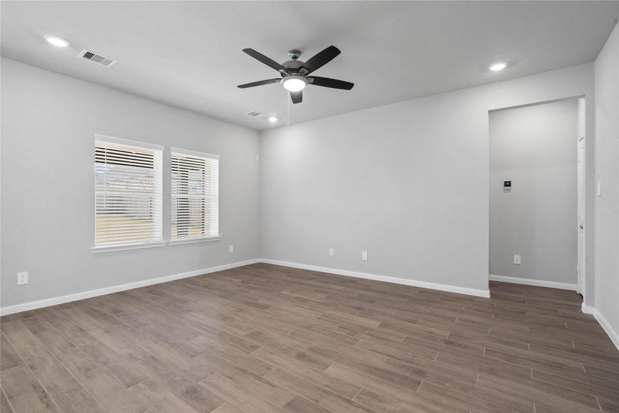 A bright and airy open-concept space featuring wood-look tile flooring, high ceilings with recessed lighting and ceiling fan, and abundant natural light from large windows (fitted with blinds).