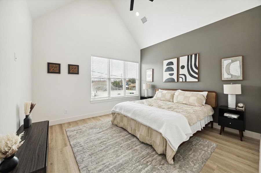 This thoughtfully designed primary bedroom features durable wood-like LVP flooring throughout. Cathedral ceilings are anchored by a stylish black ceiling fan, while oversized windows, paired with recessed lighting, illuminate the space. Enjoy breathtaking views of the downtown skyline right from your primary window.