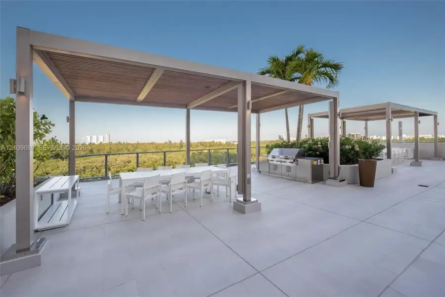 Rooftop terrace featuring large-format tile flooring, dual metal-framed pergolas with wood-finish ceilings, a built-in stainless steel outdoor kitchen, and a glass-panel railing system