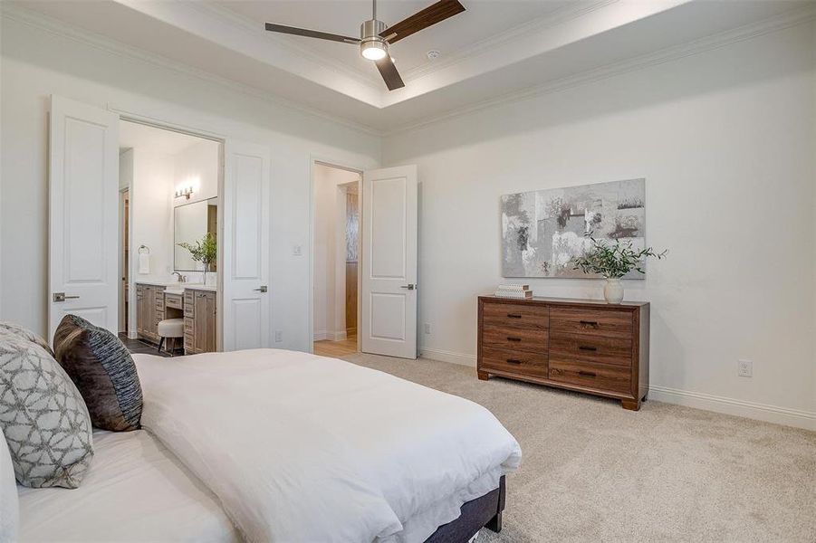 Bedroom featuring ceiling fan, a raised ceiling, crown molding, ensuite bathroom