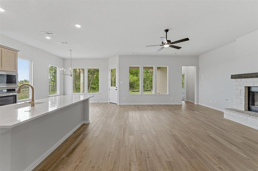 Unfurnished living room featuring a fireplace with raised hearth, light wood finished floors, suspended lighting, and a ceiling fan