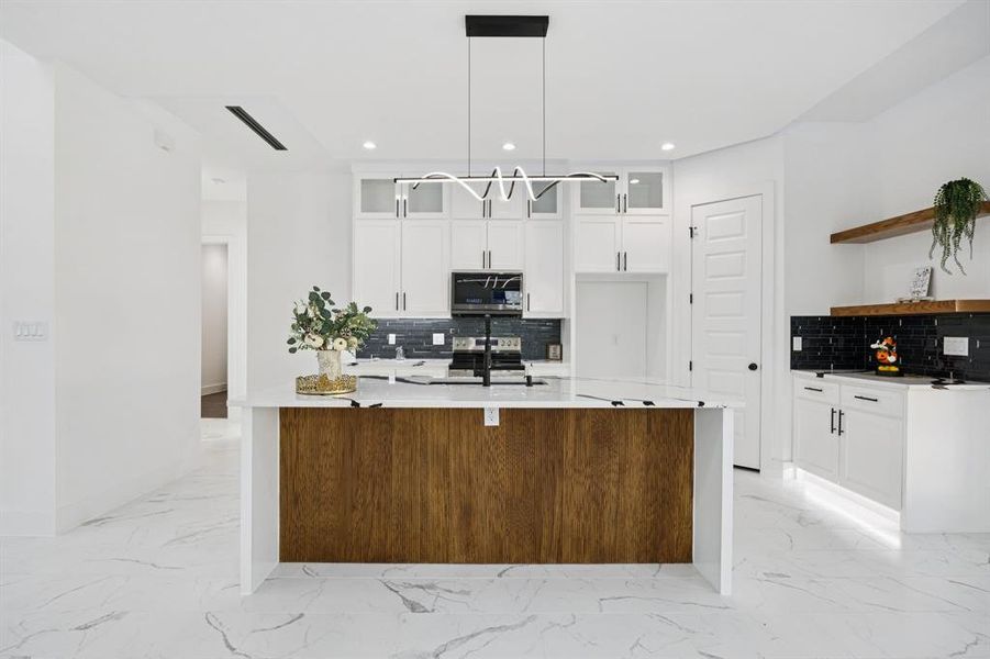 Kitchen featuring light stone counters, light marble finish floors, white cabinets, glass insert cabinets, and recessed lighting