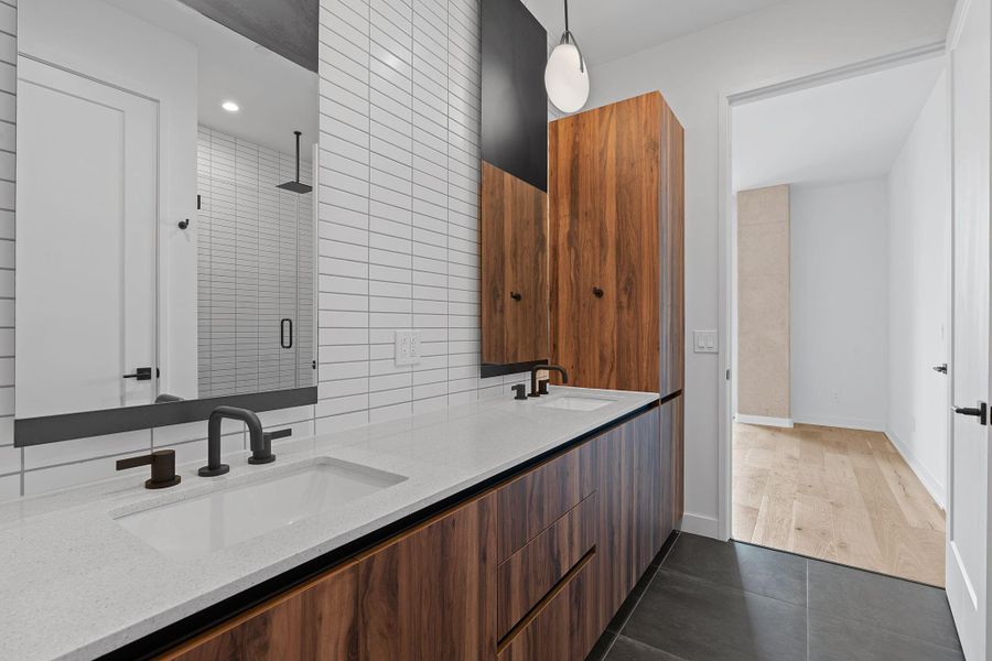 This elegant primary bathroom is equipped with high-end fixtures, a dual vanity with terrazzo style countertops, and a spacious walk in shower.