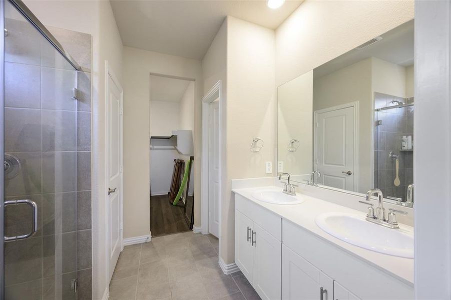 Bathroom featuring a dual vanity with white cabinetry and integrated sinks, a large wall-mounted mirror, and a glass-enclosed shower with tiled walls Bathroom featuring a dual vanity with white cabinetry and integrated sinks, a large wall-mounted mirror, and a glass-enclosed shower with tiled walls