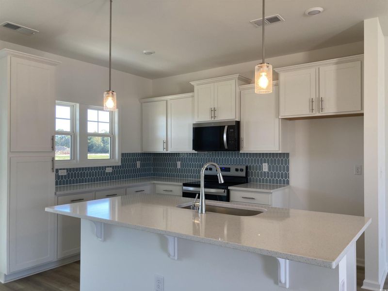 Kitchen with decorative backsplash, white cabinets, a kitchen island with sink, and stainless steel appliances