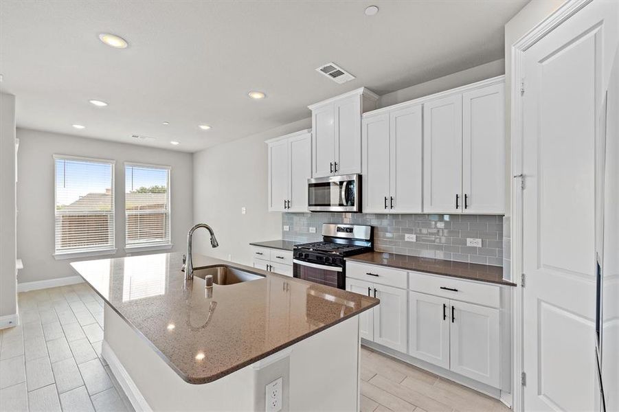 Kitchen with white cabinets, stainless steel appliances, sink, dark stone counters, and a center island with sink