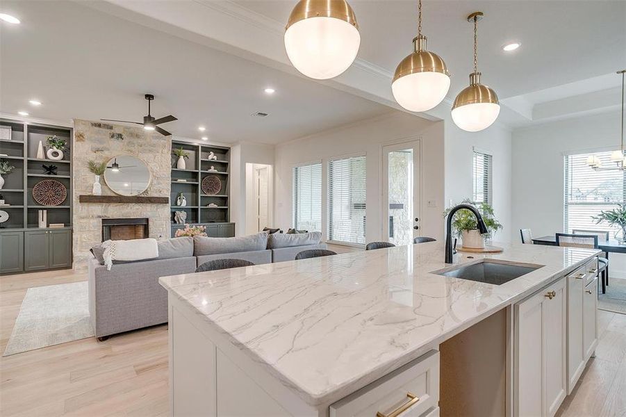 Kitchen featuring custom cabinetry to the ceiling, light hardwood floors, large island with Quartzite countertops opens to living area with built in cabinets and stone fireplace.